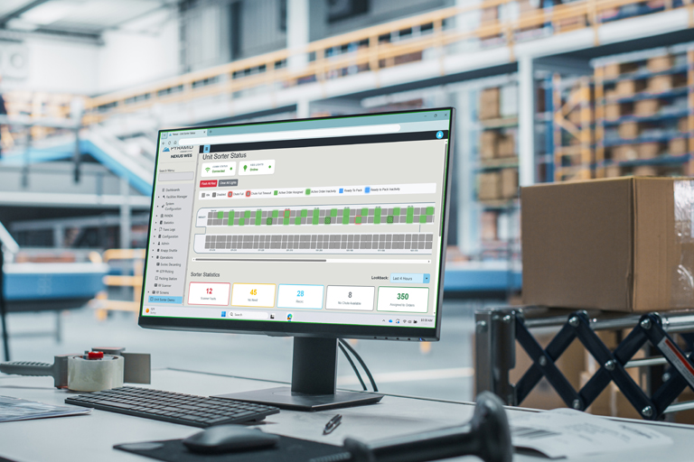 Pyramid Warehouse Execution System software on a desktop monitor managing an automated unit loop sorter in the background.